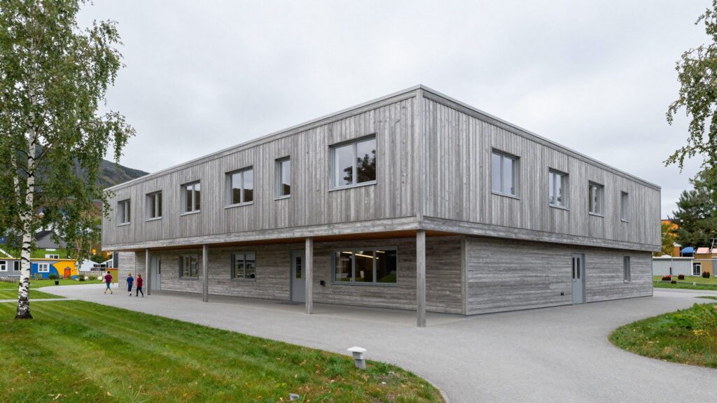 A two-storey school clad in silvery pine with a long covered walkway and birch trees.
