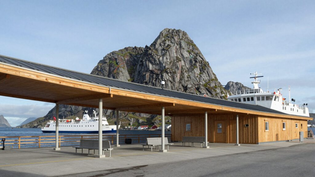 A long cantilevered timber roof over a ferry terminal, a white ferry and jagged mountains behind.